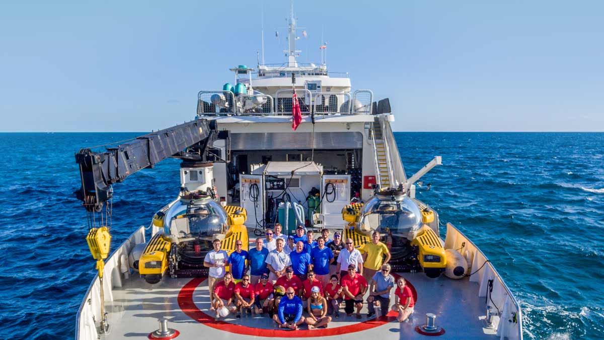 Team Triton pictured on back deck of vessel with two Triton subs in background